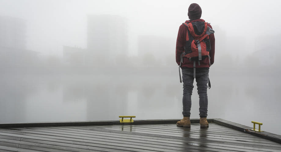A man standing on a pier on a foggy day.